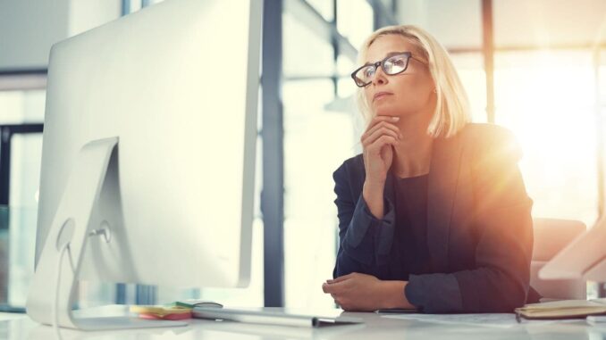 Mulher pensativa diante do computador refletindo sobre como saber se é intuição ou mente